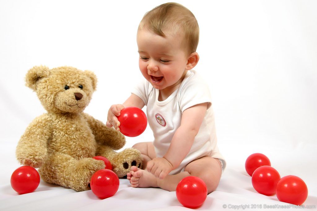 baby and her teddy playing with red balls