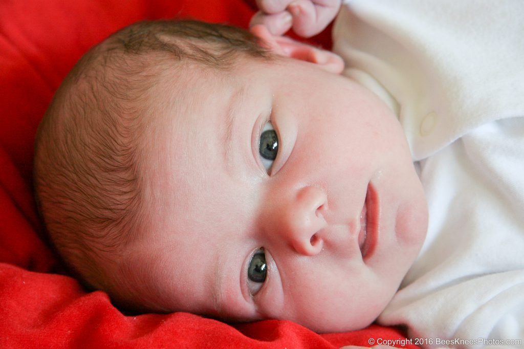 baby lying on a red blanket.