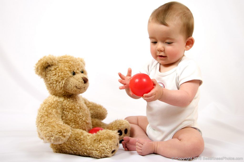 baby playing with a red ball and her teddy